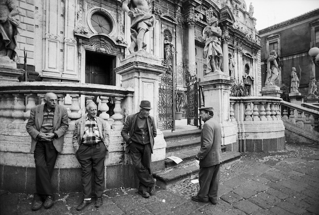 Des hommes discutant à l'entrée d'un vieux palais en Sicile