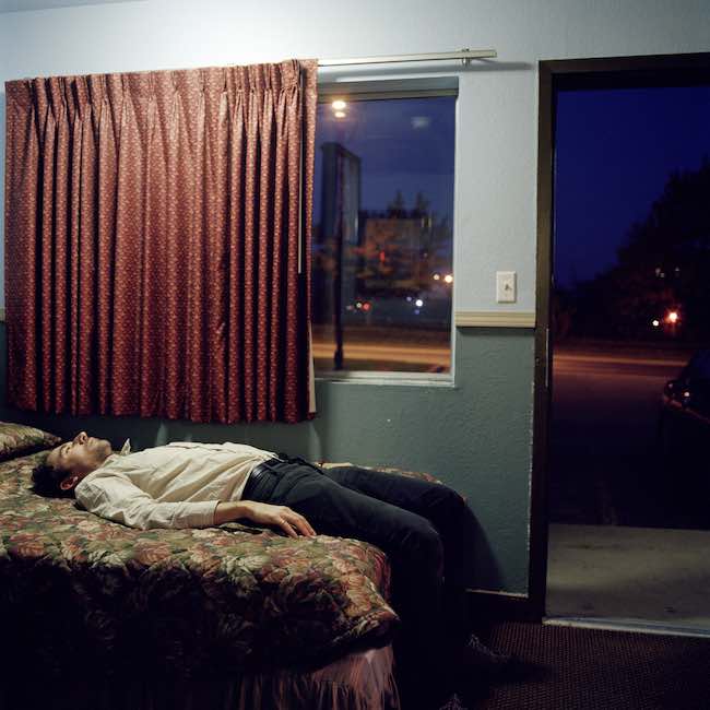 Un homme allongé tout habillé sur le lit d'une chambre d'hôtel